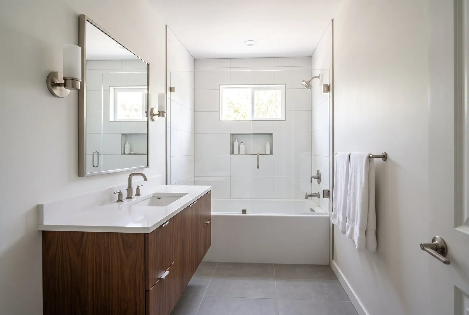 A small hall bathroom after a full remodel with a tub and shower in large white tile, a fixed glass panel and a walnut floating vanity