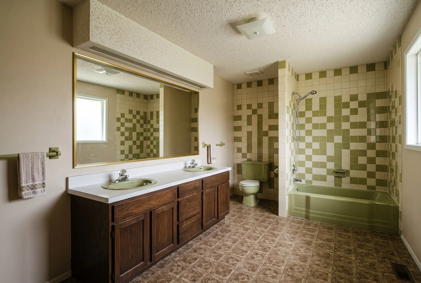 A dated 1970s bathroom with green tile, a matching green tub and a long double vanity