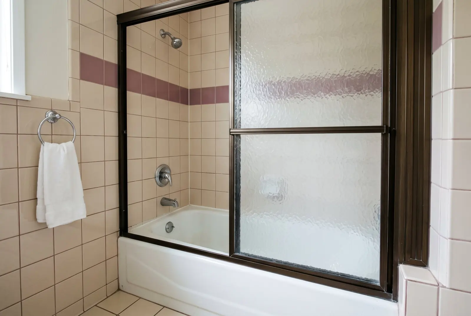 A 1980s tub alcove with small square tile and a framed sliding glass door