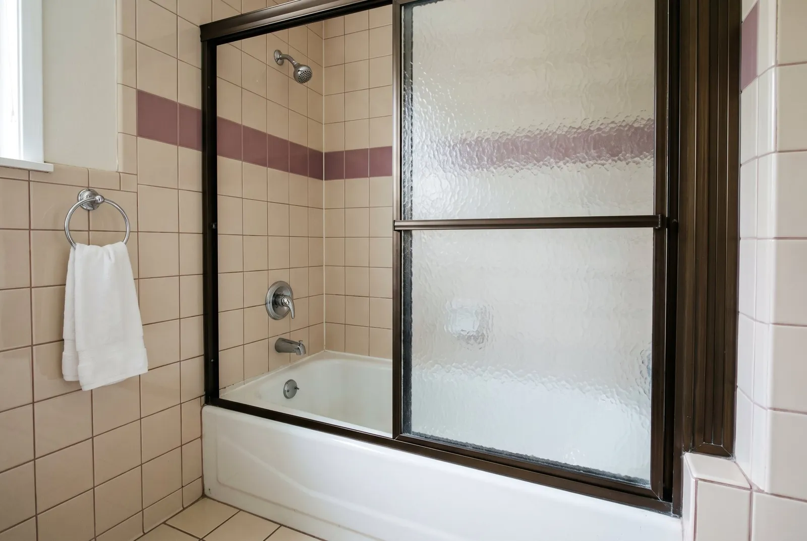 A 1980s tub alcove with small square tile and a framed sliding glass door