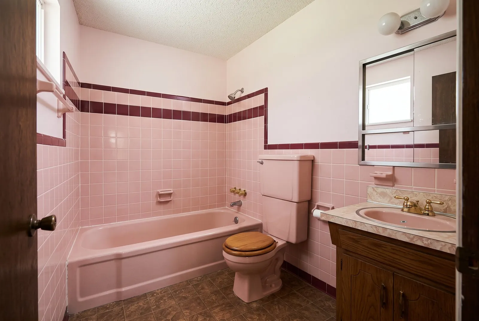 An original 1970s bathroom with pink tile, a pink tub and a tall tank toilet